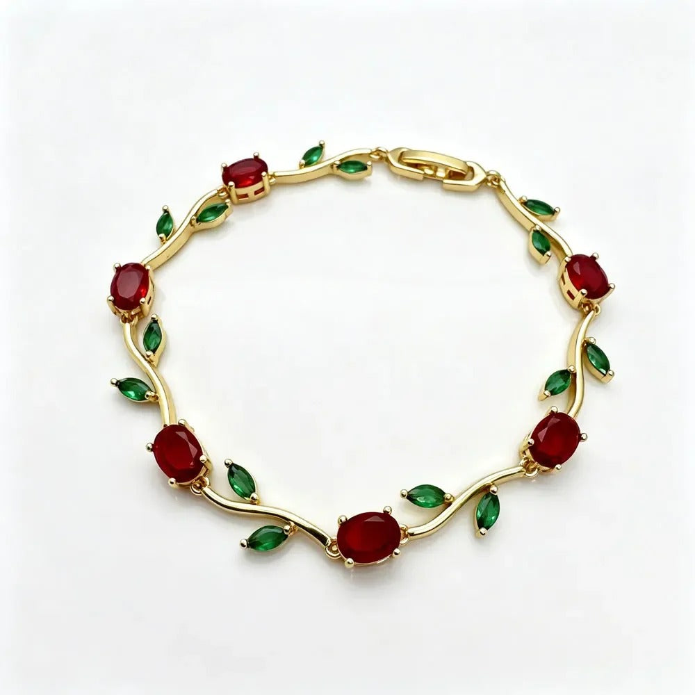 A gold vine-style bracelet featuring oval red gemstones and small green marquise-cut accents, displayed on a clean white background. sasha jewels 