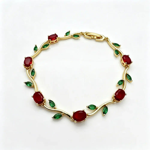 A gold vine-style bracelet featuring oval red gemstones and small green marquise-cut accents, displayed on a clean white background. sasha jewels 